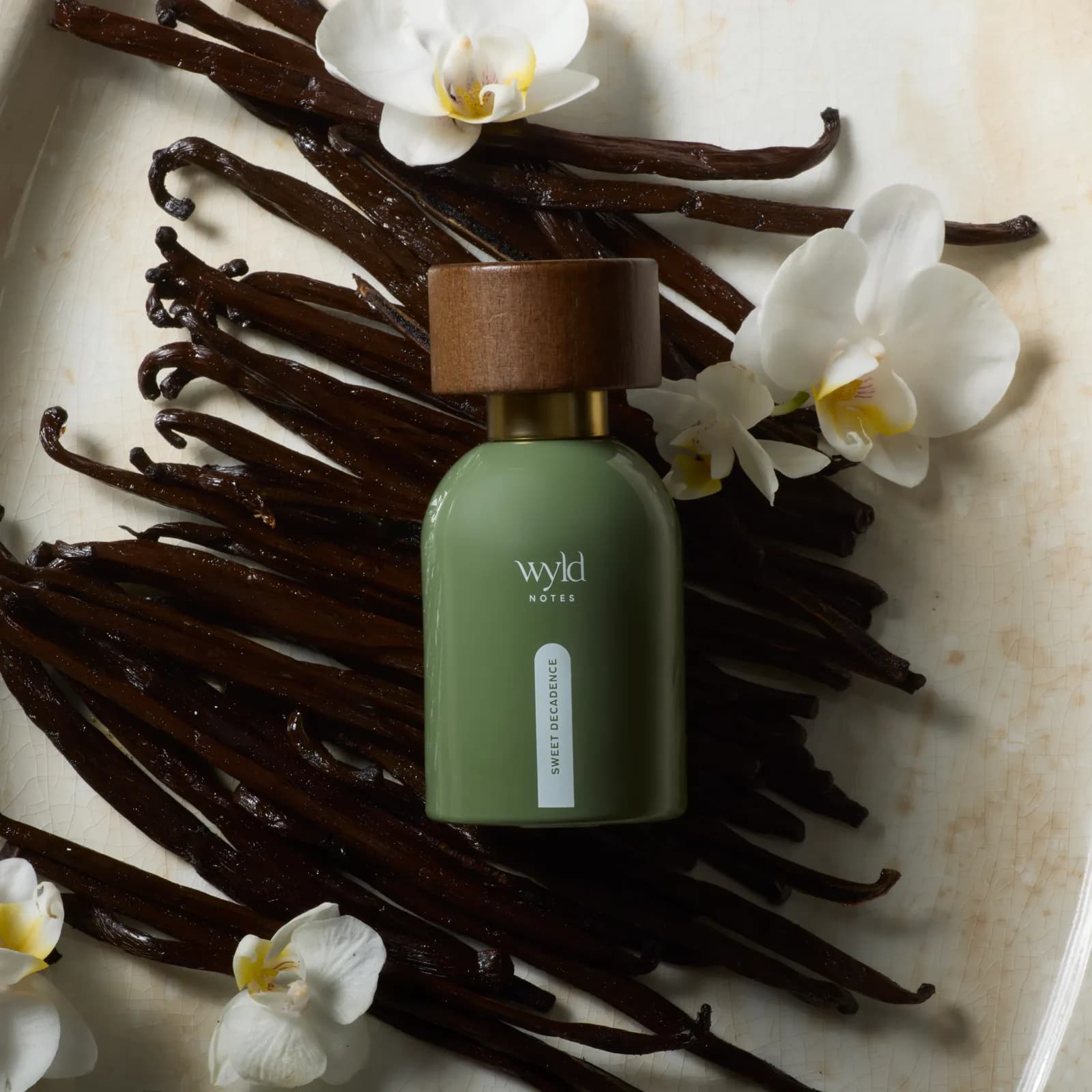 Sweet Decadence von Wyld Notes liegend zwischen Vanilleschoten und weißen Orchideen