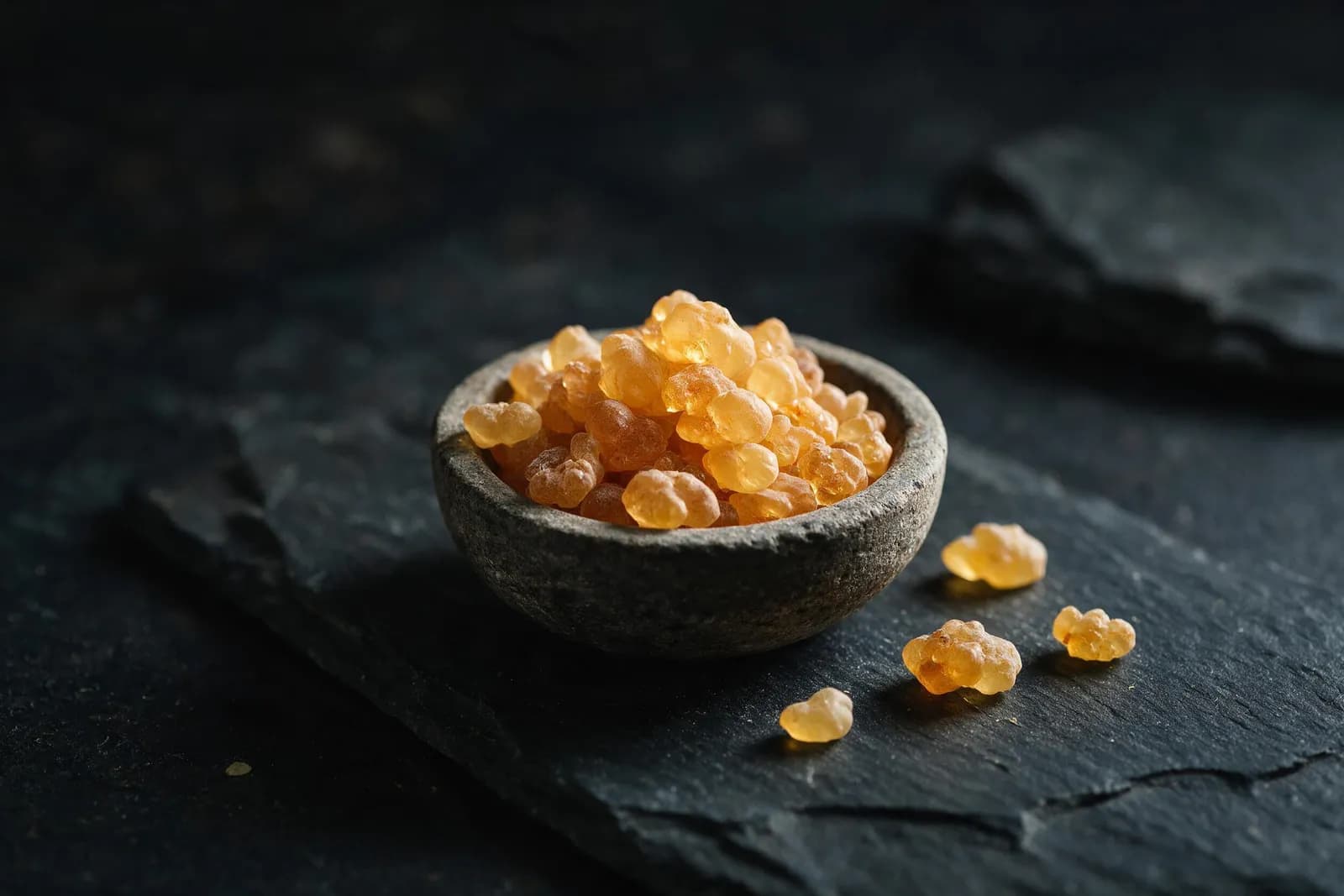 Goldene Weihrauch-Tränen in einer kleinen Steinschale auf dunklem Schiefer