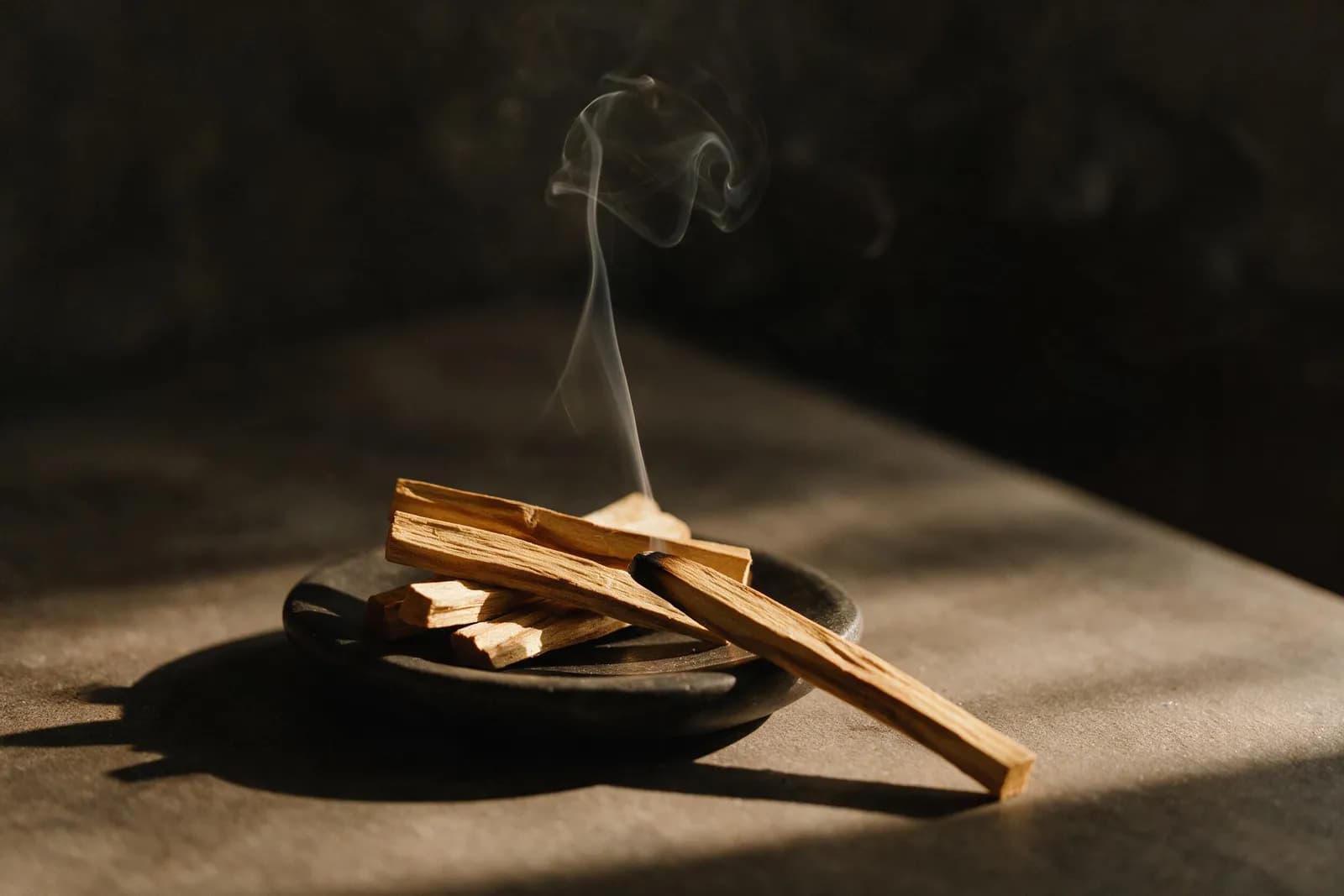 Palo-Santo-Hölzer auf einer Steinschale, von einem der Stäbe steigt ein feiner Rauchfaden auf