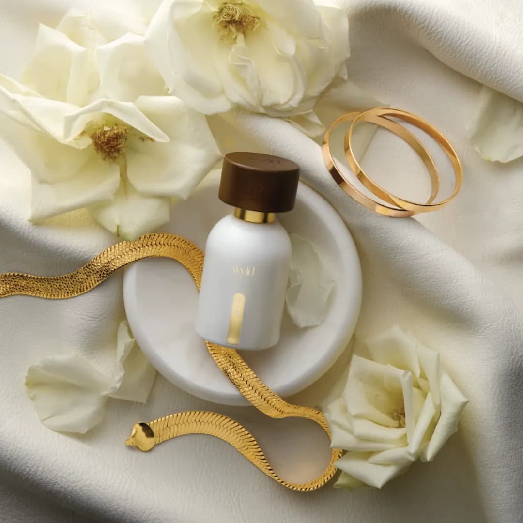 White Lie von Wyld Notes liegend zwischen weißen Rosen und einem Goldarmband